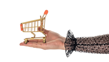 A hand holding a miniature gold shopping cart against a black backdrop