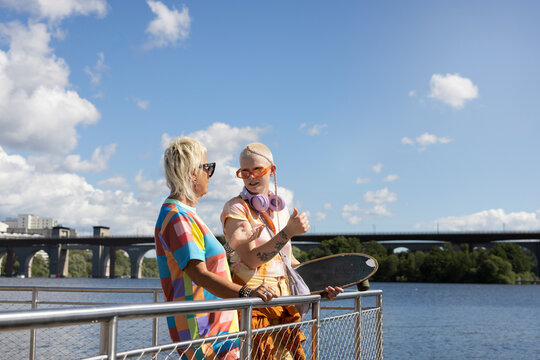 Young woman discussing with female friend while standing near railing at sunny day
