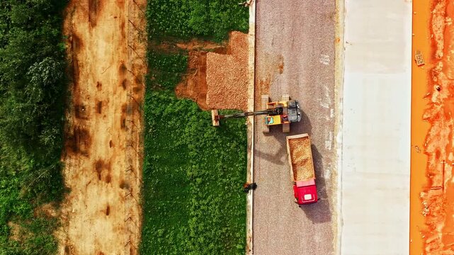 Top-down view of Excavator spreading gravel on railway construction slope with dumper truck nearby