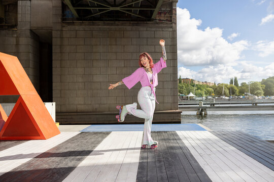 Portrait of young woman posing with roller skate on jetty under bridge against cloudy sky
