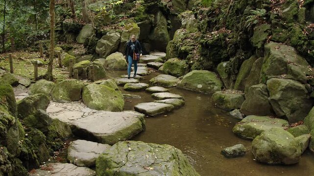 Caucasian woman walks on step stones in mossy rock grotto in green park