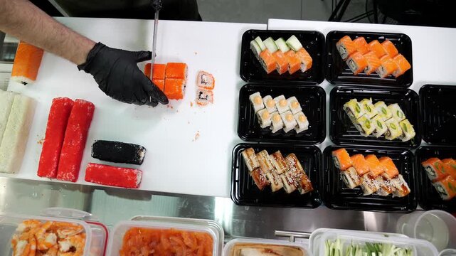 Top view of the sushi chef's work in a Japanese restaurant, the chef cuts a lot of sushi on the table in the restaurant's kitchen. Sushi with salmon, salmon, shrimp, avocado.