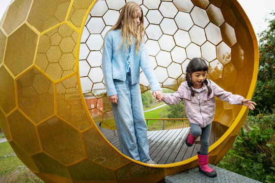 Girl stepping outside yellow sphere while holding hands of sister