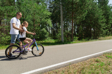 Obraz premium Child trying the bicycle. Happy father with daughter are having fun in forest at summertime.