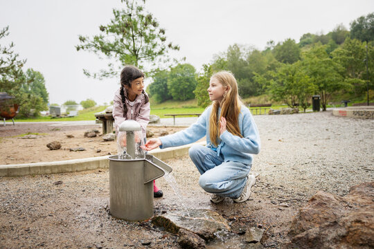 Sisters washing hands from fountain at park