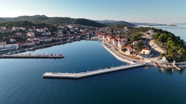 Drone flies over Sali harbor pier and marina at sunset, showing the small fishing village turned tourist town on Dugi Otok, Croatia with scenic Adriatic views.