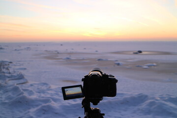 The lake is covered with ice, an evening winter landscape, the camera is in the foreground