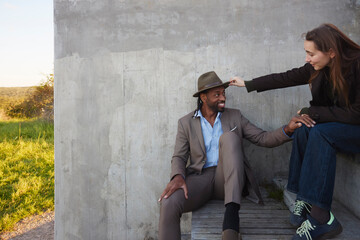 Woman adjusting hat of man sitting on steps near wall