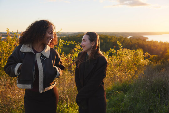 Happy female friends talking with each other standing on hill