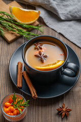 Sea buckthorn herbal tea in a black cup on a wooden background with spices
