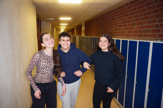 Happy male and female friends standing with arm in arm near lockers