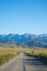 Perspective view of a gravel road going through fields towards a distant mountain range under a clear blue sky