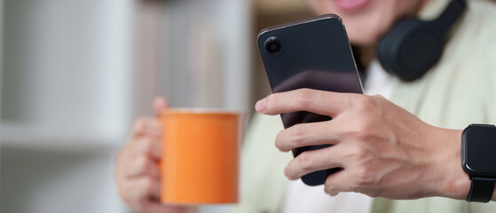 Digital Lifestyle. Young man holding smartphone and coffee cup in a cozy home setting.