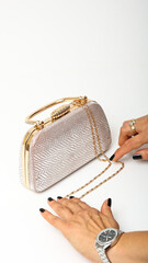 Top down view of elegant rose gold evening clutch bag with gold hardware and textured finish. Luxurious box purse with a metallic handle and delicate chain strap, handled by female hands.