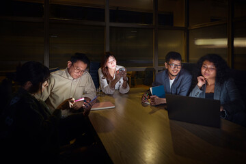 Female business experts using wireless technologies while sharing strategies with male colleagues during office meeting at night