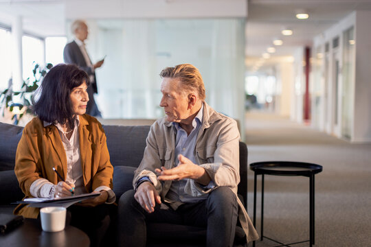 Senior businessman discussing strategy with female colleague while sitting on sofa in office
