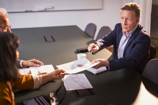 High angle view of senior businessman passing document to female colleague in meeting at office
