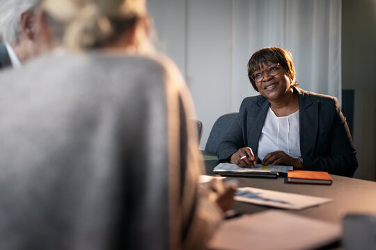 Smiling mature female business expert listening to colleague in office meeting at board room