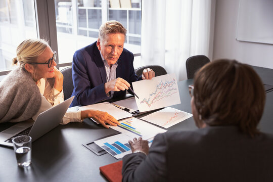 Senior businessman showing progress report to colleagues while discussing in meeting at office