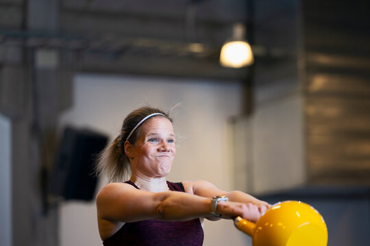 Dedicated woman lifting heavy kettlebell while doing strength training in gym
