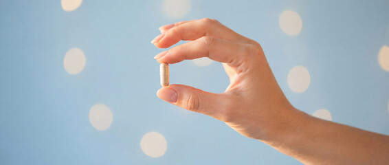 Hand holding a single capsule pill against soft blue background with bokeh lights, symbolizing healthcare, wellness, medicine, and supplements