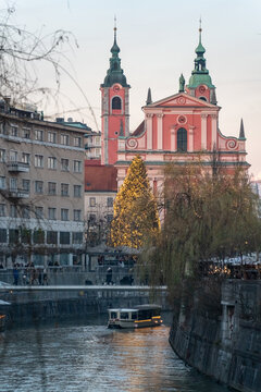 Christmas-lit view of the Franciscan Church and a riverboat floating along the Ljubljanica River in central Ljubljana, Slovenia at clody weather 
