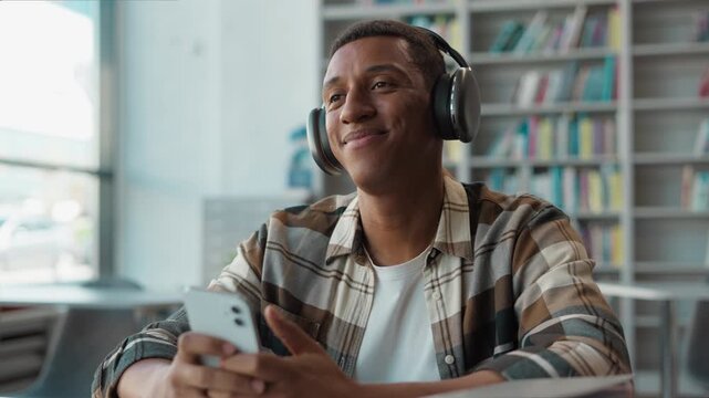 Happy African American man relaxed student listening music headphones using smartphone university library enjoying audio learning study focus smile mobile phone device male guy college relax education