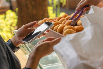 customer paying with smartphone while buying fresh donuts at local bakery stall