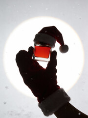 Silhouette of Hand in Santa Glove Holding Red Perfume Bottle Against Bright Circle