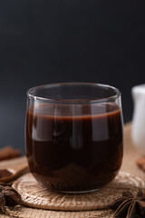 Hot chocolate in glass and star anise and cinnamon sticks on black background