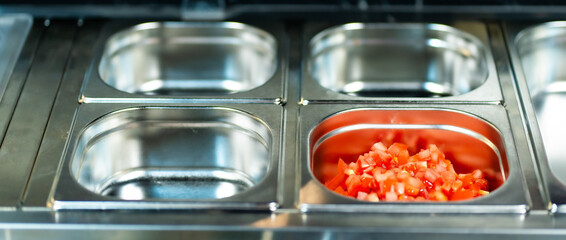 Metal containers filled with various sliced vegetables and ingredients in a professional kitchen setting
