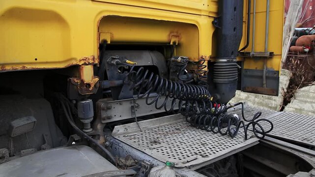 Detailed shot of pneumatic and electrical connections behind cabin of industrial transport vehicle. Air lines and wiring harness extend across checker plate platform, revealing weathered surface