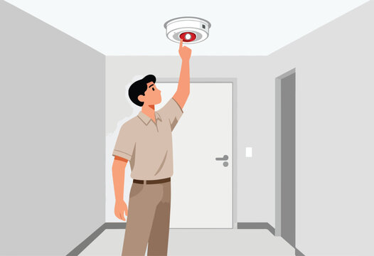 Man pressing button on ceiling smoke detector in a hallway