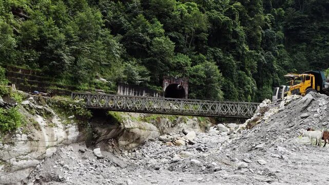 Static shot of a bailey bridge over a silt laden mountain river showing the geometric pattern of the steel beams and the rushing water passing underneath the structure.