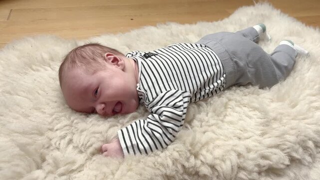 A baby lying on its stomach on a sheepskin and trying to raise its head