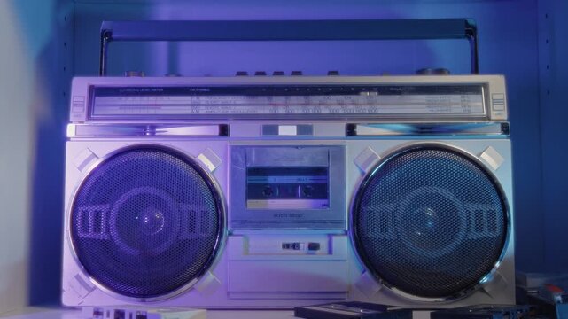 A Man Gently Slides A Compact Cassette Into A Vintage 1985 Boombox While Resting On A Cozy Sofa, Enjoying Warm Neon Lighting And Immersing Himself In Retro Music And Nostalgic Living Room Atmosphere