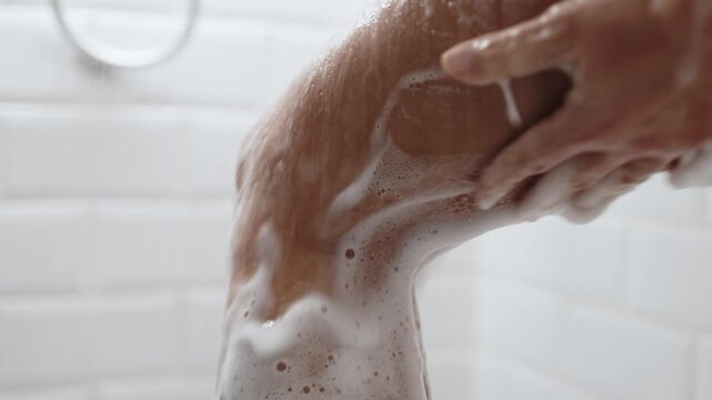 A close-up of a person washing his foot in the shower, showing the soapy lather and running water. Hygiene concept.