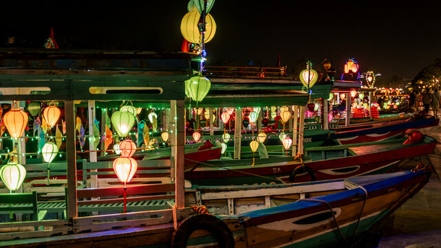 Colorfully decorated boats with lanterns waiting along the riverbank in Hoi An, Vietnam at night.