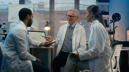 Medium long shot of senior Caucasian male scientist teaching young multiethnic assistants or students in modern laboratory office, showing chemical reaction rates on laptop screen - Powered by Adobe