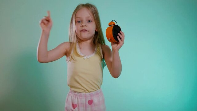 Funny girl in a T-shirt and shorts sets the time on the alarm clock. The child holds the clock in her hands and smiles.