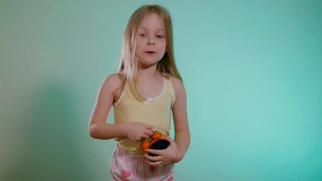 Funny little girl in a pajama top and shorts is scared looking at the alarm clock - she overslept and is late. Surprise of the child when she looked at what time it was.