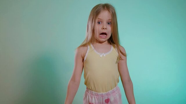 Funny little girl in a pajama top and shorts is scared looking at the alarm clock - she overslept and is late. Surprise of the child when she looked at what time it was.