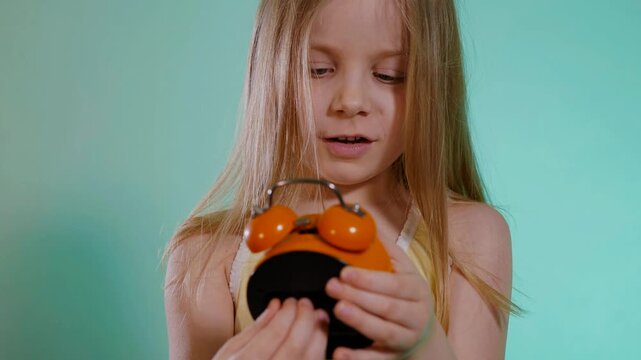 Funny girl in a T-shirt and shorts sets the time on the alarm clock. The child holds the clock in her hands and smiles.