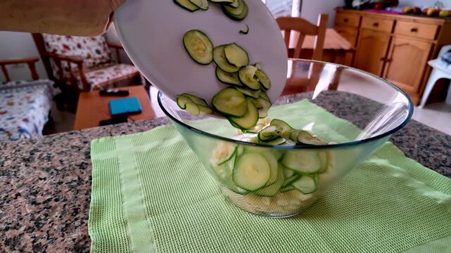 Man's hands adding freshly sliced zucchini into a transparent glass bowl with Italian pasta, preparing a delicious and healthy Mediterranean diet meal with typical and genuine products at home