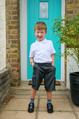 Happy and excited little boy outside the front door to his home on his first day of school wearing his uniform and short trousers, UK © Alex Segre