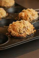 Golden brown muffins close up with a crumble topping cooling down in muffin tin. Homemade cupcakes just out of the oven with crumbly top. Home baking sweet treat food snacks. Vertical portrait photo