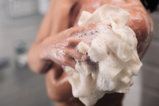 Close-up of a person in a shower using a loofah with soap bubbles, showcasing personal care and hygiene routine in a modern bathroom environment with soft lighting