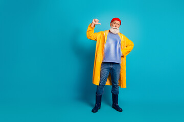 Man in yellow raincoat with striped shirt poses confidently in blue studio