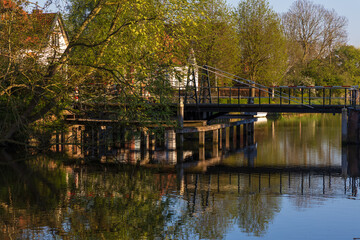 Fototapeta premium Old drawbridge over a tranquil canal in Bedum, Groningen, Netherlands. Bright spring morning, reflections of trees and houses in the water, idyllic scene