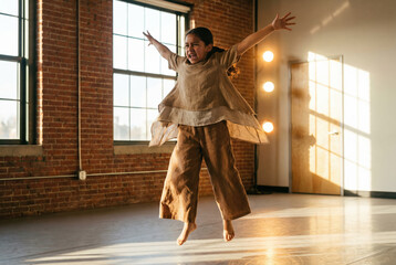 Ni&ntilde;a expresando emoci&oacute;n en salto durante pr&aacute;ctica de danza contempor&aacute;nea en estudio iluminado.